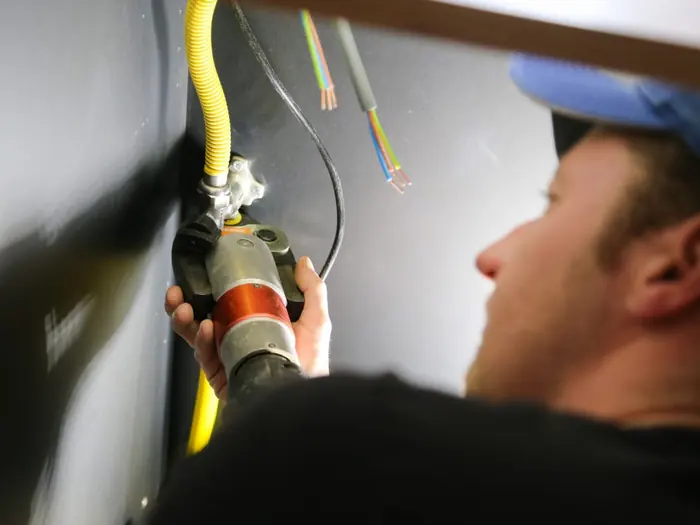 Monteur werkt met een gele installatiebuis en losse draden bij een inbouwdoos
